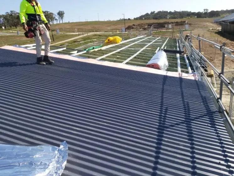 Roofer in hi-vis installing dark metal roof sheets