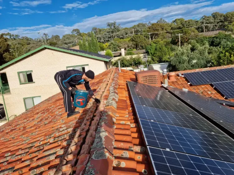 Roofer inspecting a terracotta tile roof beside solar panels